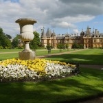 An image of a English country garden with a water fountain in the foreground and a castle in the background.